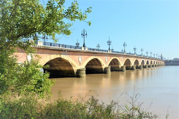 Une photographie réaliste et professionnelle de la ville de Bordeaux montrant ses monuments caractéristiques et son architecture emblématique : la Cité du Vin avec sa structure moderne distinctive, les façades classiques du centre-ville, la Garonne en premier plan ou arrière-plan, l'atmosphère urbaine vibrante du centre historique avec ses bâtiments en pierre de taille aux couleurs chaudes, et idéalement une vue qui capture l'essence touristique et monumentale de Bordeaux comme métropole régionale du Sud-Ouest français. Image sans texte ni logo visible.